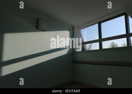 Window frames cast sharp shadows on the floor. Minimalist room feels calm and quiet. Natural light enhances quiet interior space Stock Photo