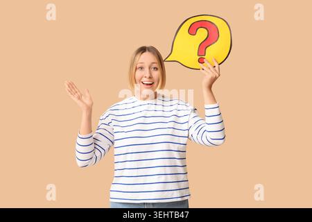 Surprised adult woman holding speech bubble with question mark on beige background Stock Photo