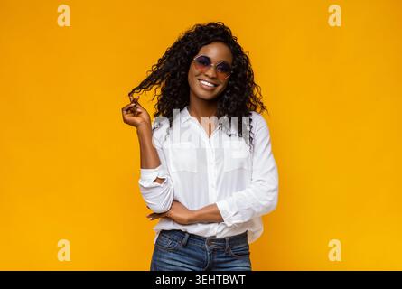 Young Woman in Sunglasses Poses Confidently Against a Vibrant Yellow Background Stock Photo