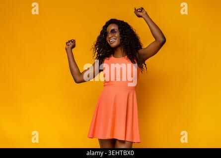 Joyful Woman Dancing in a Bright Orange Dress Against a Yellow Background Stock Photo
