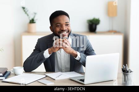 Smiling black businessman daydreaming at workplace in office Stock Photo