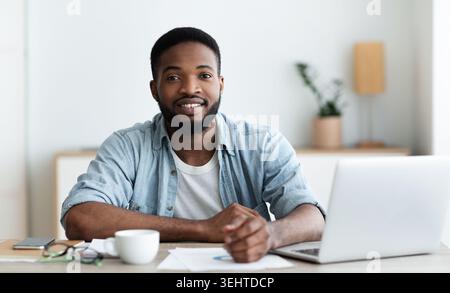 Smiling african american worker looking at camera, sitting at workplace Stock Photo
