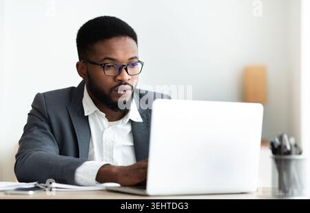 Serious black businessman working on laptop in office Stock Photo