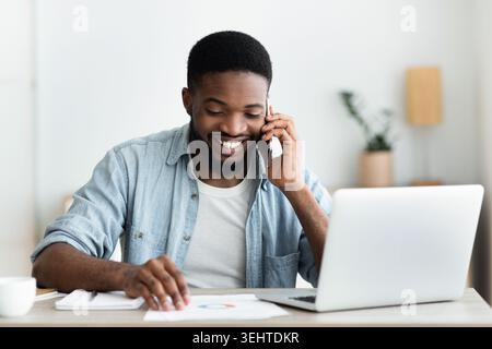 Cheerful african businessman checking financial reports and talking on phone Stock Photo