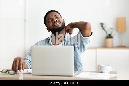 Black man suffering from neck pain while working on laptop Stock Photo