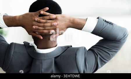 Man in Formal Attire With Hands Clasped Behind Head, Sitting in a Relaxed Posture at Office Stock Photo