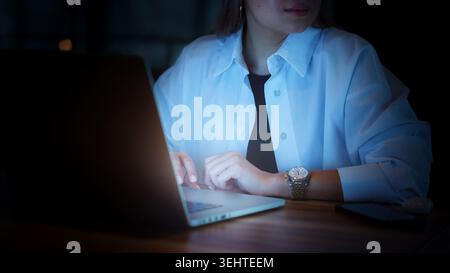 Woman working on laptop at night in dark room with focus on hands and watch Stock Photo