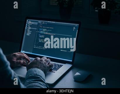 Person works on computer in dark room while writing code for web application or software project Stock Photo
