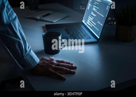 Person working late at night on a laptop with a coffee cup on the table Stock Photo
