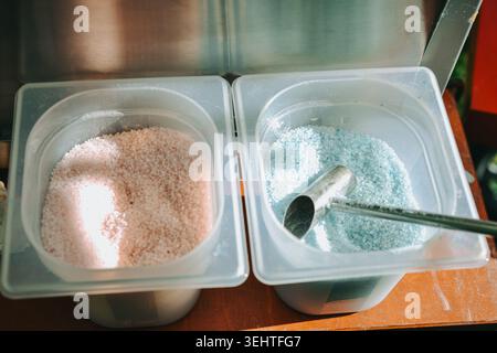 Close up of pink and blue flavored popcorn seasoning salts in plastic containers with metal scoops beside a concession machine. Ideal for cinema snack Stock Photo