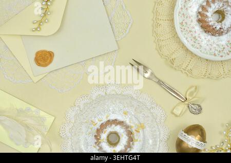 Yellow, single color Easter, pastel table decoration with Easter cakes, golden egg, elegant fork, an envelope and yellow card to fill with content. Stock Photo