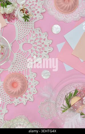 Top view pink, Easter table decoration with Easter eggs, flowers, feathers, cupcake tins, crochet tablecloth, letters and glass plates. Stock Photo