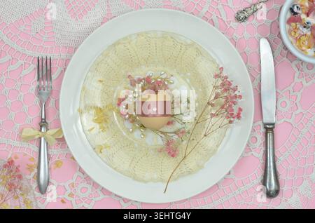 Table setting for Easter: top view elegant decorations: yellow crocheted napkin, pink background,  Easter egg on white plate, retro fork and knife. Stock Photo