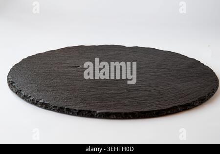 Empty black round slate serving board on white background with rustic kitchen presentation and minimal food backdrop Stock Photo