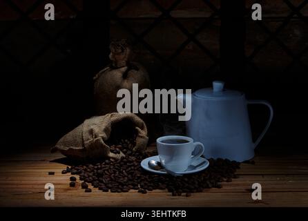 Steaming Hot Coffee with White Ceramic Teapot and Burlap Sacks of Roasted Coffee Beans on Rustic Wood Stock Photo
