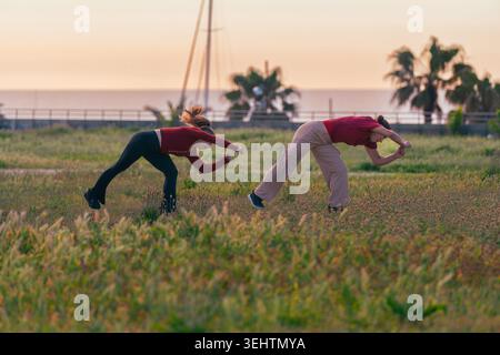 Two active women practicing contemporary dance and expressive movement in a grassy field at sunset. Stock Photo