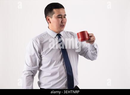 Young Asian businessman holding coffee mug and looking thoughtfully away Stock Photo