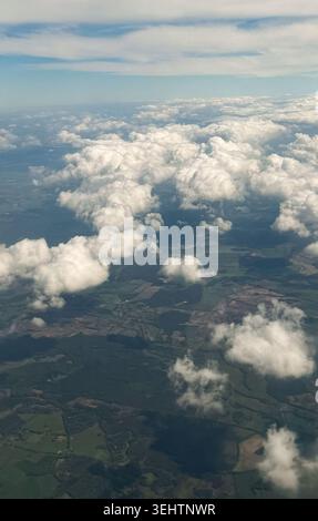 Aerial view of fluffy white clouds above green fields and patches of farmland under a bright blue sky with scattered clouds in the background Stock Photo