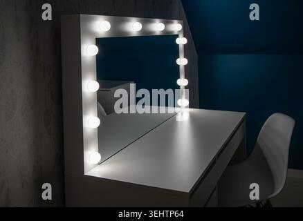 White modern vanity table with light bulbs illuminated in a dark room in home blue color wall bedroom. Stock Photo