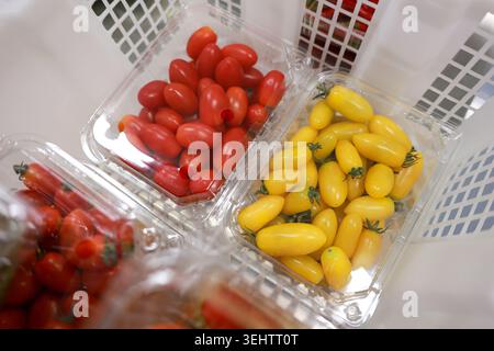 Fresh red and yellow cherry tomatoes in clear plastic containers sitting inside white shopping basket displaying healthy organic vegetable choice Stock Photo