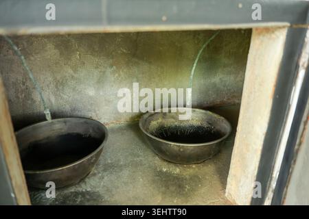 Old dark metal cauldron resting inside empty rustic concrete fireplace niche creating eerie quiet abandoned gloomy feeling in historical kitchen archi Stock Photo