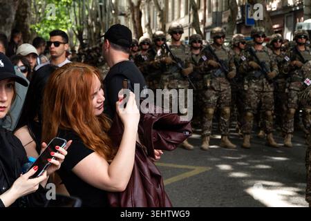 Soldiers in camouflage stand at attention on a city street while civilians observe and take photos with their phones. Stock Photo