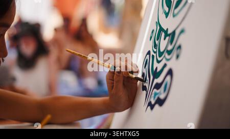 Artist focusing on painting calligraphy on canvas, showing creativity and detail in art Stock Photo