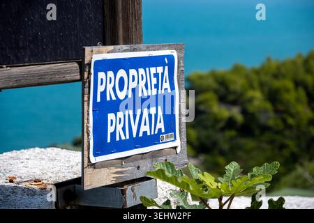 Vieste - Apulia - Italy - 08-29-2025: Blue sign reading PROPRIETA PRIVATA is fixed to weathered wood, with turquoise sea and green trees softly blurred in the background. Stock Photo