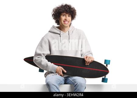 Guy holding a longboard and sitting on a panel isolated on white background Stock Photo