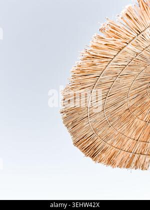 Beach sun umbrella made of woven straw with fringed edge, close up natural texture on a neutral sky background, summer seaside vacation detail Stock Photo