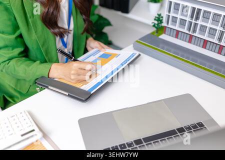 Real estate consultant explaining property financing and home purchase costs in office, presenting calculator, keys, and housing model to support mort Stock Photo