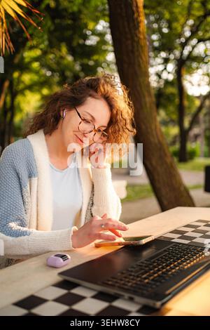 Woman working remotely outdoors using laptop and smartphone Stock Photo