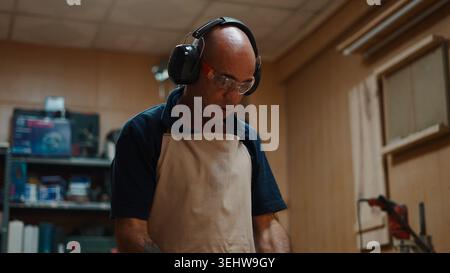 Carpenter wearing safety gear and apron working with wood in workshop Stock Photo