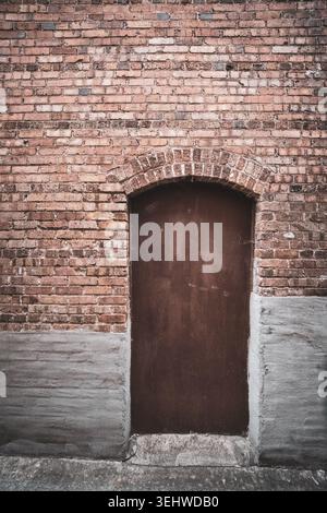 Boarded up wooden arched door in a weathered brick wall Stock Photo
