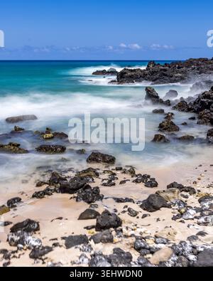 Motion blurred ocean waves washing rocks on beach Stock Photo