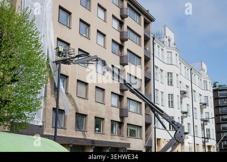 Construction worker on hydraulic lift platform repairing residential apartment building facade in urban area Stock Photo