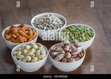 Nuts of different varieties lie in bowls on a wooden table, top view. Assortment of nuts and pumpkin seeds, sunflower seeds, cashews and almonds nuts Stock Photo