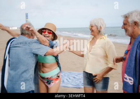 Joyful senior friends hugging and laughing on beach vacation Stock Photo
