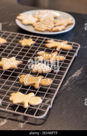 Decorated gingerbread cookies cooling on metal rack on dark stone counter with white icing details Stock Photo