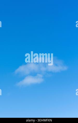 A vertical low angle view of an isolated fluffy white cloud floating in a vibrant clear blue sky Stock Photo