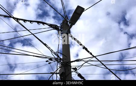 Low-angle view of a vintage street lamp surrounded by a messy tangle of electrical power lines against a cloudy sky. Stock Photo