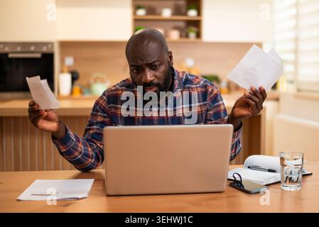 Anxious black man reviewing financial documents and calculating his expenses. Stock Photo