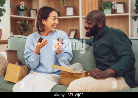 A multiracial couple relaxes on the couch, reviewing an online order as they unpack a freshly delivered perfume. Stock Photo