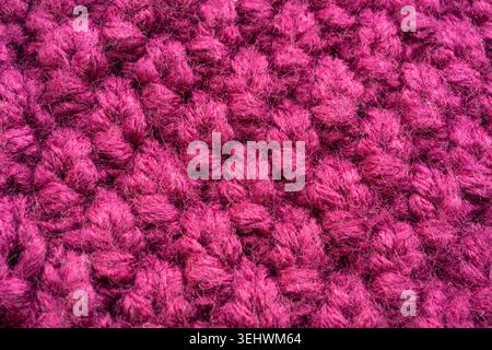 Knitted woolen fabric pattern in rich magenta. Macro texture of a cozy sweater, thick woven yarn threads. Soft and fluffy knitwear design with a bold, Stock Photo