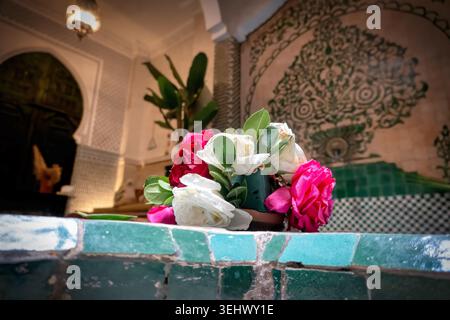 A fresh bouquet of pink and white roses rests on a green tiled fountain inside a traditional Moroccan riad courtyard. Stock Photo