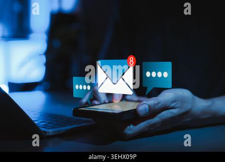 Email notification communication concept showing hand using smartphone with unread message alert, chat bubbles, and laptop for online messaging, Stock Photo