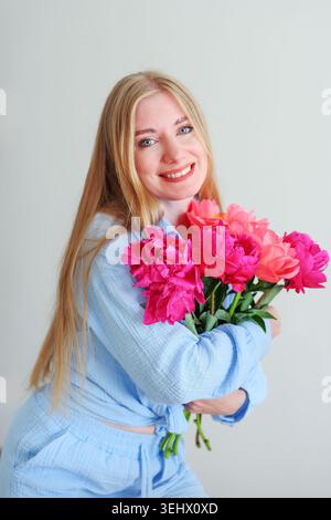 Elegant female portrait with pink peonies and blue outfit, romantic spring fashion style and cheerful positive emotions. Stock Photo