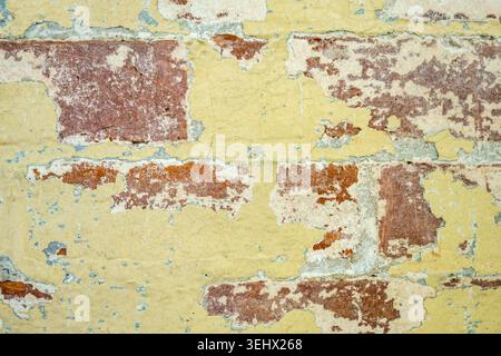 Close up view of rustic brick wall with peeling yellow paint. Stock Photo
