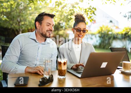 Business colleagues collaborating on laptop at outdoor cafe Stock Photo