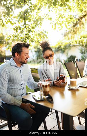 Colleagues collaborating on smartphone during outdoor business meeting Stock Photo